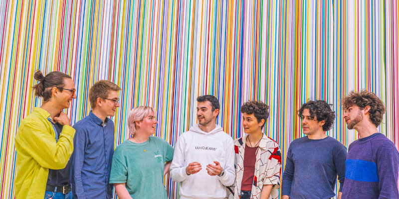 A group of students standing and talking in front of a colourful piece of artwork