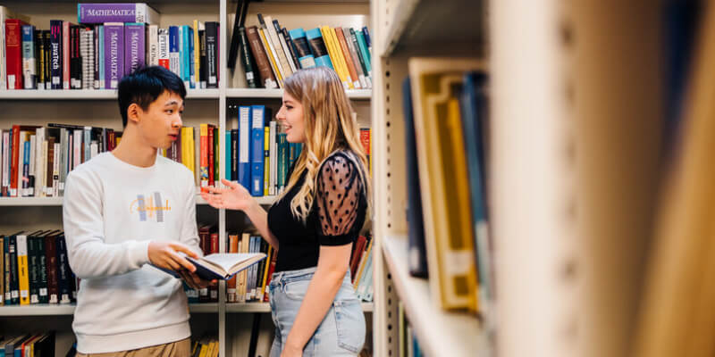 Two students in discussion, standing in a library