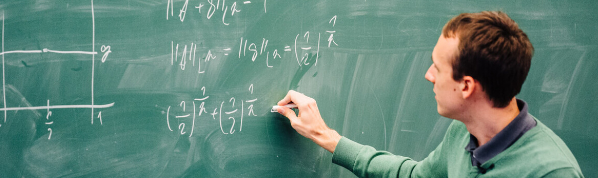 A lecturer writing mathematical equations on a chalk board