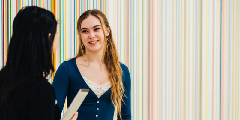 Two female students talking in front of some colourful artwork