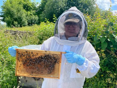 A picture of me in a white beekeeping  suit holding a frame from a beehive. 