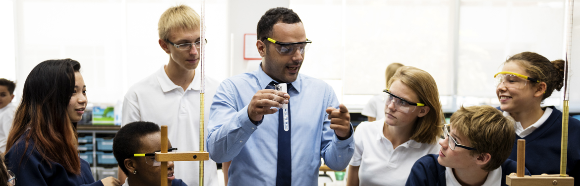 Image of male teacher holding test tube in science lab surrounded by pupils