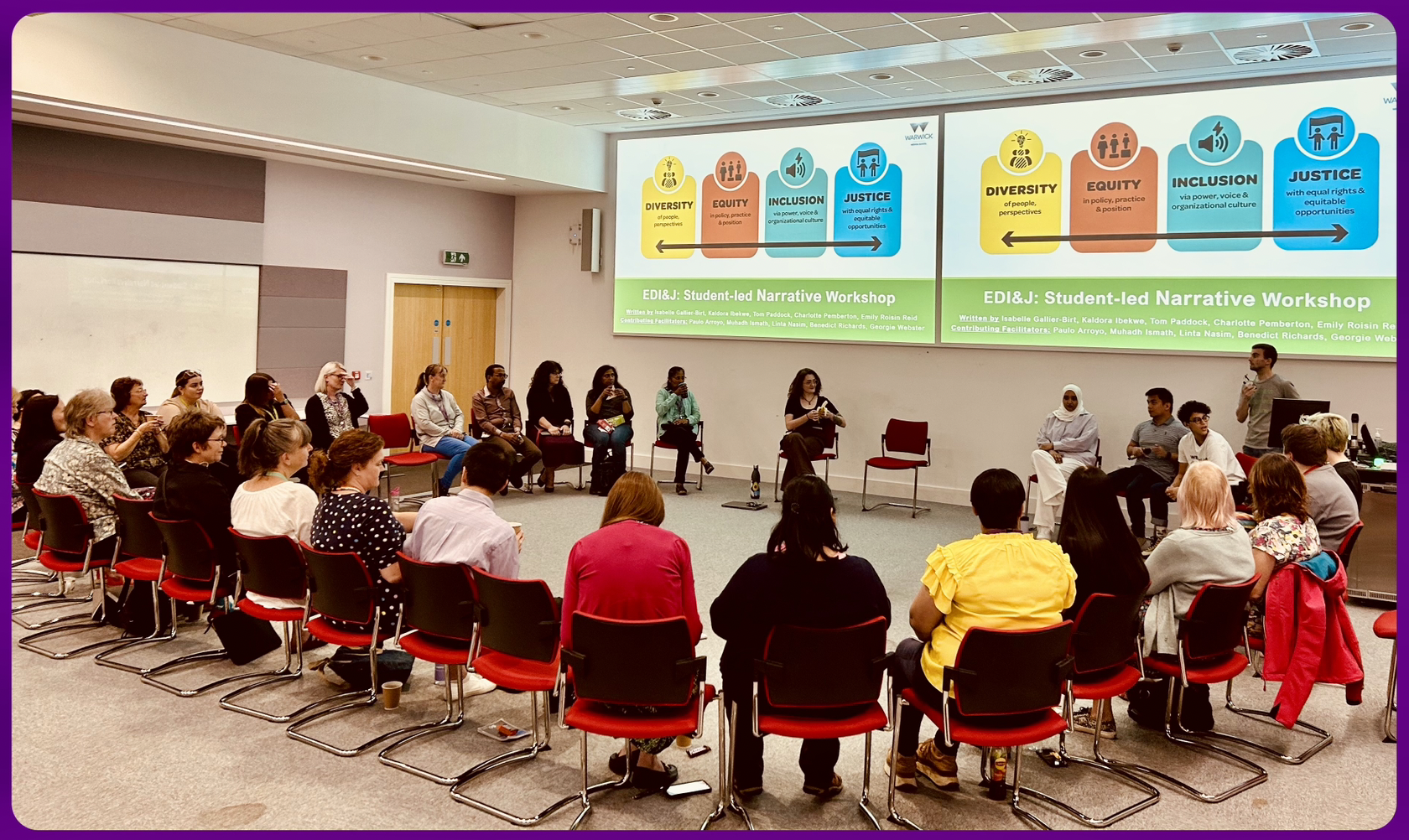 A group of seated staff gather around student facilitators in a circle, looking at EDIJ title slide
