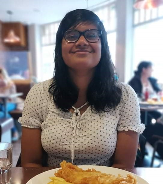 Photograph of Poppy smiling in a restaurant with a plate of food in front of her.