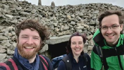 3 people (The author and two friends) standing in front of the Slieve Gullion Passage Tomb