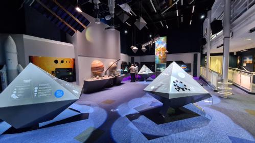 An exhibition area with a number of interactive tables, and large scale models of planets on the left-hand wall