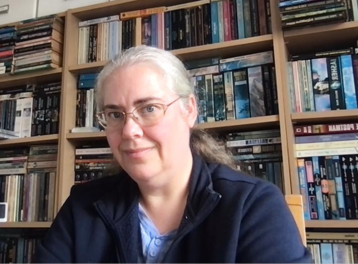Head and shoulders of Elizabeth Stanway, sitting in front of a bookcase full of books.