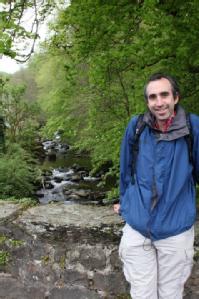 Ben McMillan leaning against a stone bridge, above a verdant welsh river gully