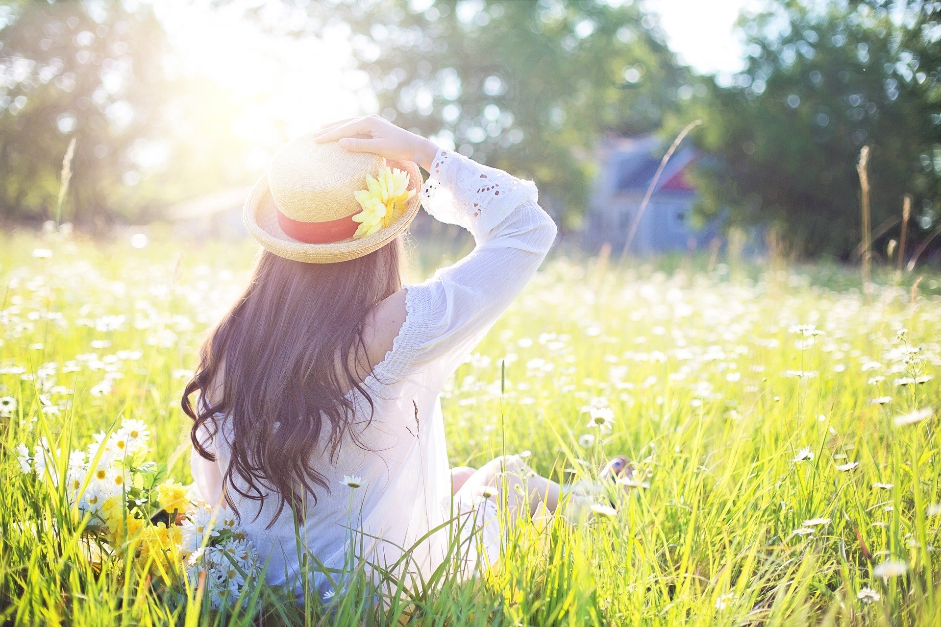 woman with a sunflower in her hat sat in a field of grass on a sunny day