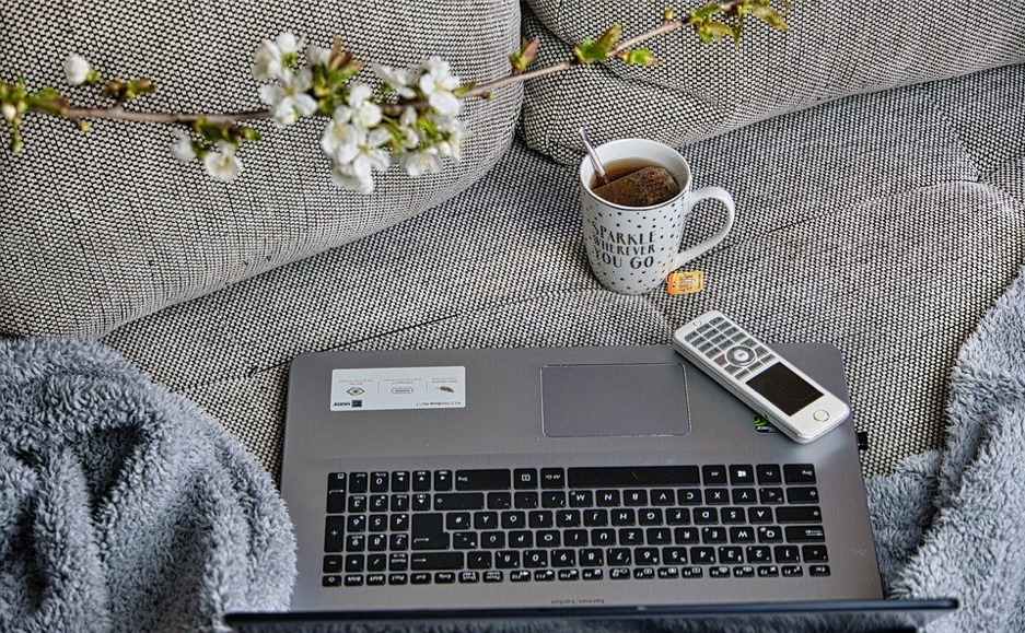 Image of a laptop and mobile phone placed on a sofa, next to a cup of tea