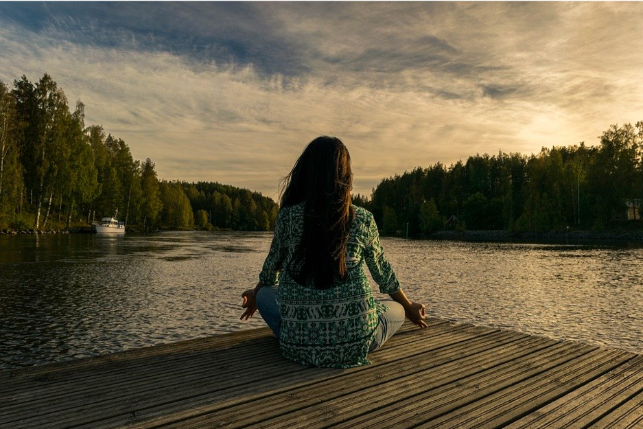 Picture of a woman seated on a dock overlooking a bay meditating