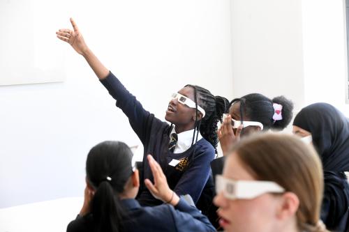 A group of young women trying out a scientific experiment. They are wearing white glasses for this. One is pointing into the air in excitement.