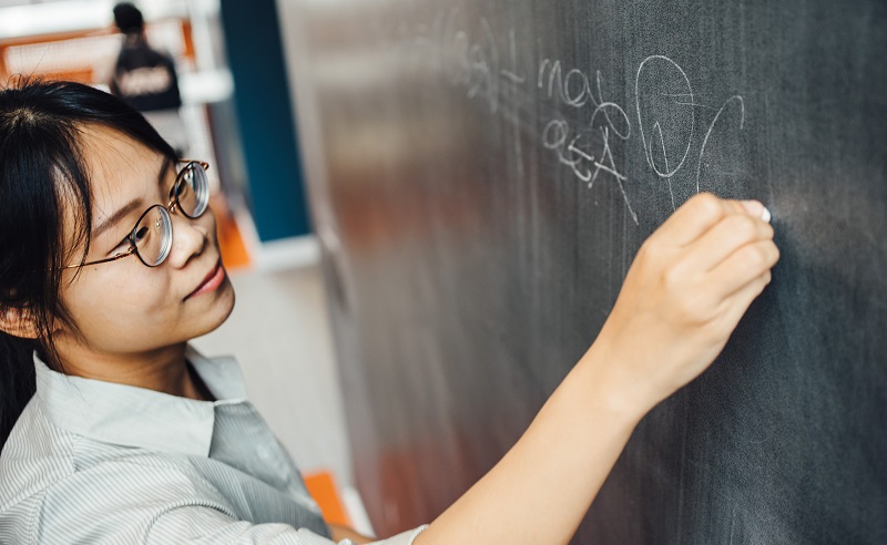 A student writes equations on a chalkboard.