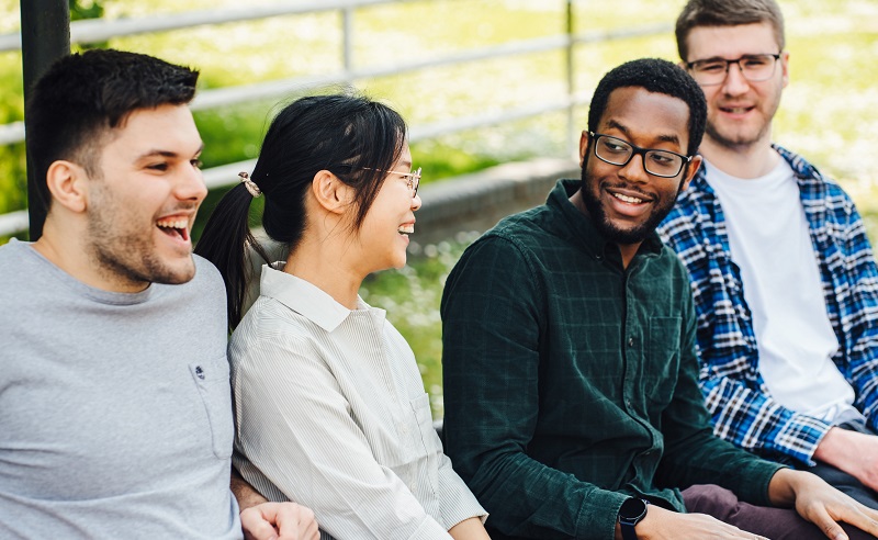 Students sit outdoors, chatting and laughing.