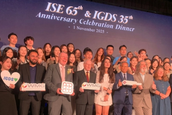 A diverse group of people, including academics and students, celebrate the anniversary of an education programme by cheering and holding signs on a stage