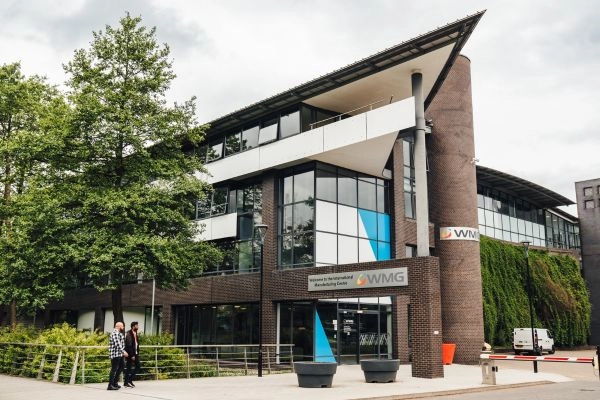 Exterior of a modern academic building with a glass and brown brick façade, featuring WMG signage at the entrance.