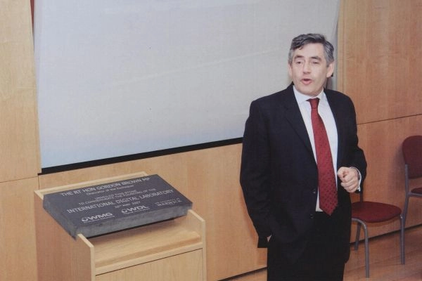 Former UK Prime Minister Gordon Brown speaks whilst standing next to a grey foundation stone for the IDL building