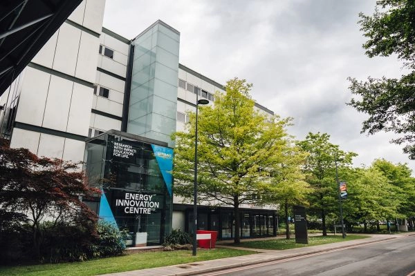 Exterior view of the Energy Innovation Centre, featuring a glass façade and WMG branding, with trees lining the road