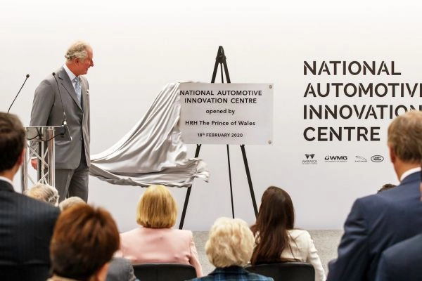 A plaque on an easel is unveiled at the formal opening of the National Automotive Innovation Centre, with an audience seated facing the stage.