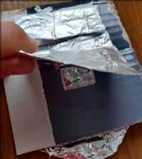 On the other side of the cardboard another piece of foil is taped down on one side of the foil so that it can be lifted up as a flap.