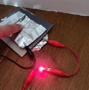 A wired up version of the pressure sensor with a lit LED - a finger is pressing down on the foil to complete the circuit
