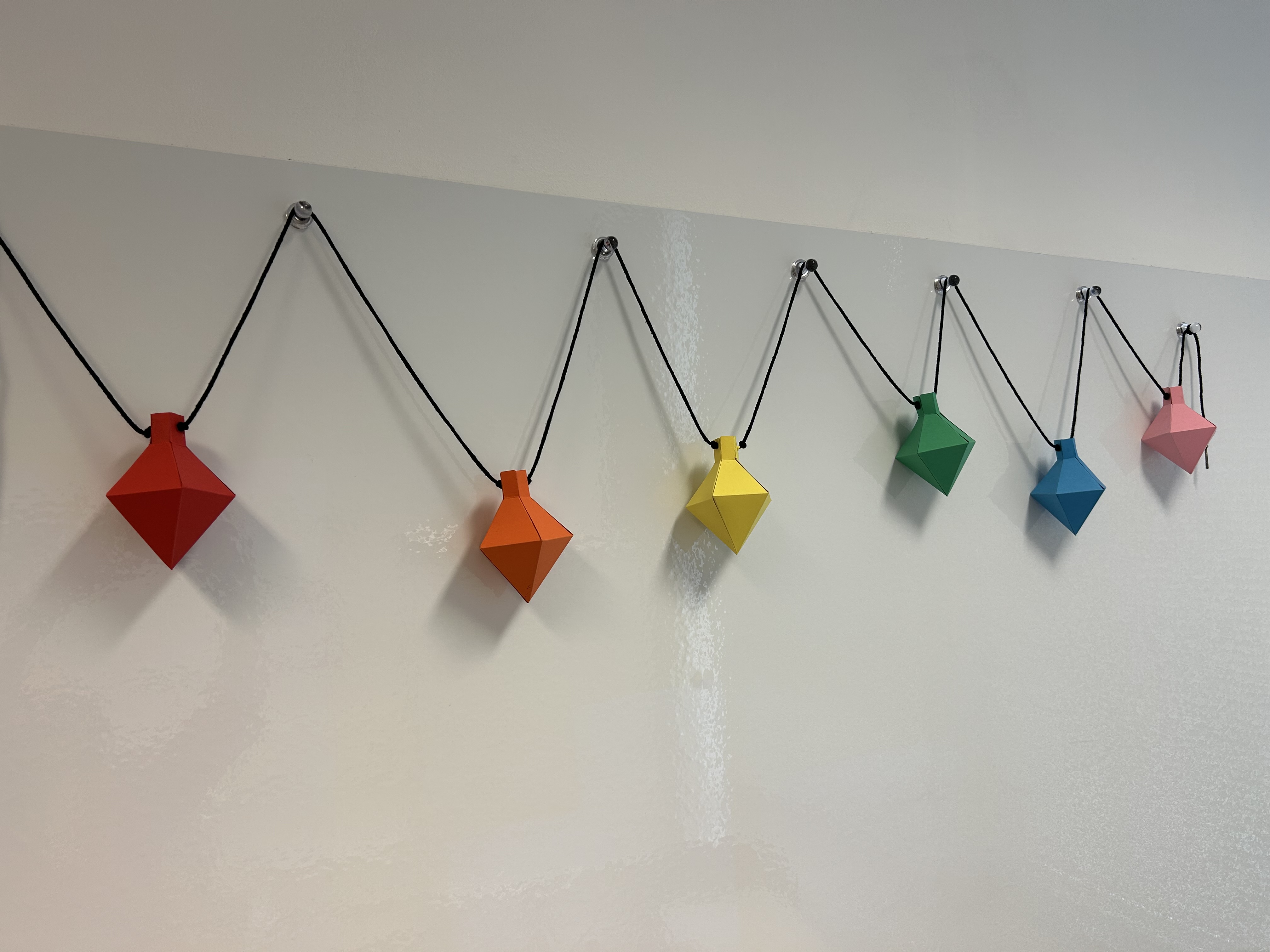 A row of paper lanterns that have been folded out of flat sheets of paper. They are all in bright colours following the rainbow.