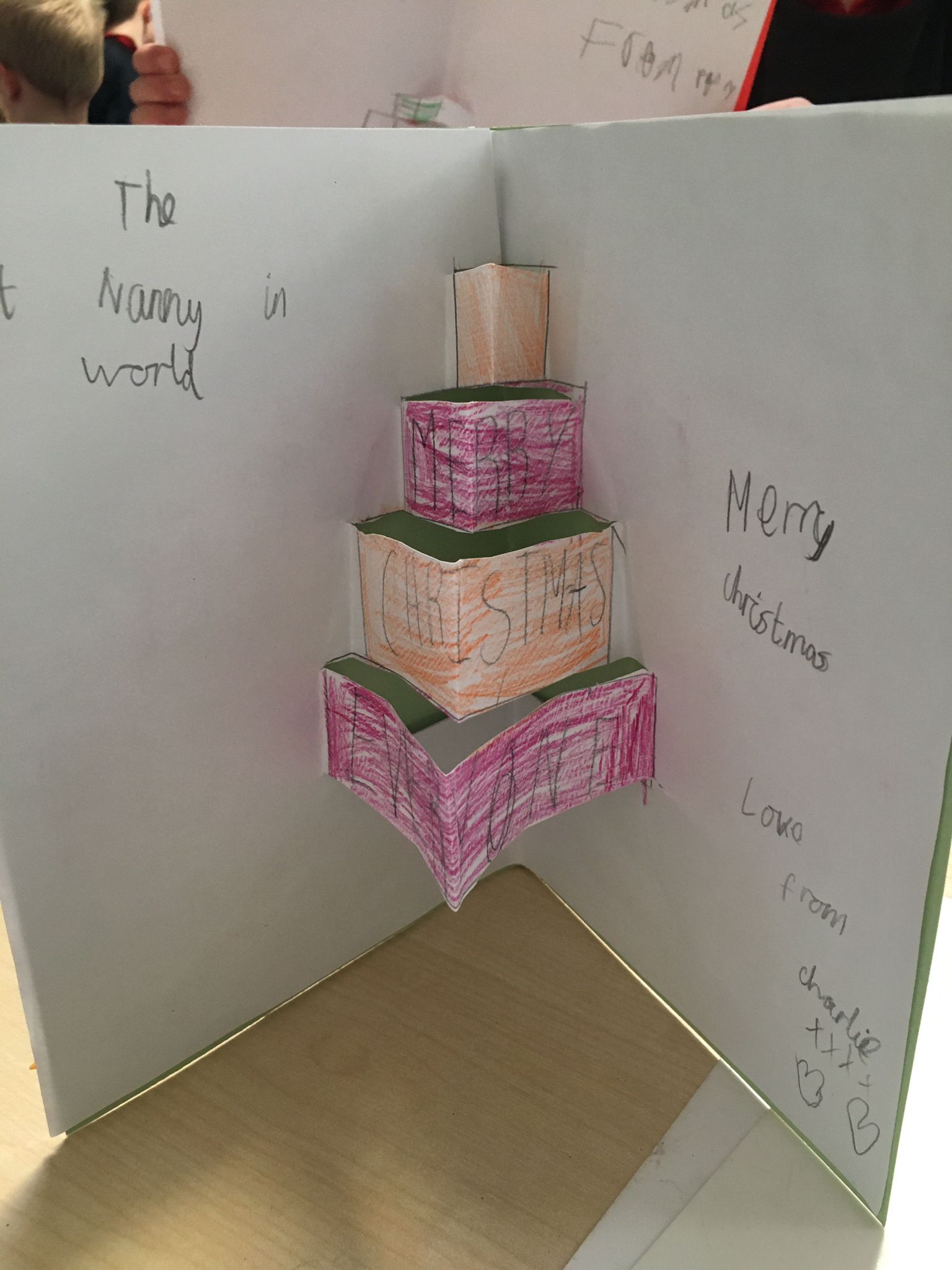 A pop up card designed and made by a primary student to celebrate Christmas. It shows three boxes popping up out of the card as if they were stacked up.