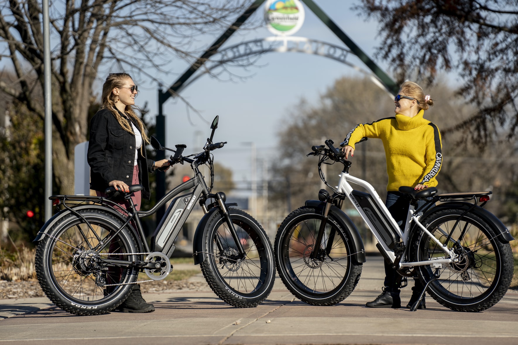 Two people are holding e-bikes