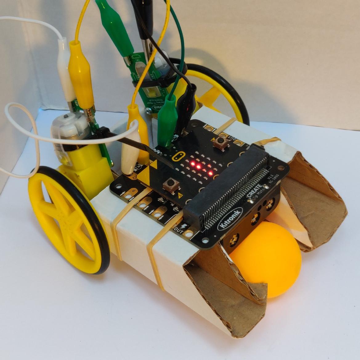 A picture of a vehicle kit with a cardboard chassis and a micro:bit controller