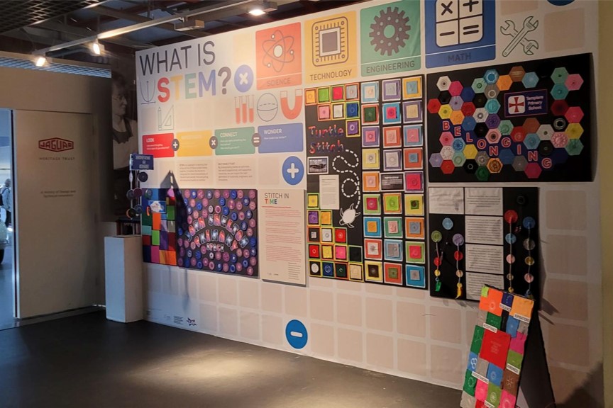 A photo of the gallery showing the work done by children in local schools on the Stitch in Time project. There is a wall with 'What is STEM' along with samples of the childens work. 