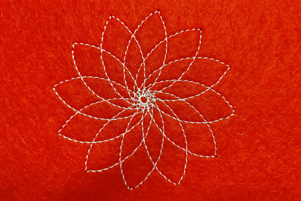 A flower made up of petals rotating around the centre. The flower is stitched using white thread on red felt.