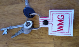 a white leatherette key fob with the letters w m g stitch on it in red. It is joined to a key ring with keys on it. 