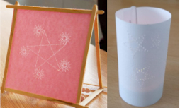 red paper in a frame with holes in it in the shape of stars with many points. White paper standing in a cylinder shape, with holes in it in the shape of stars. Light glows through the papers.