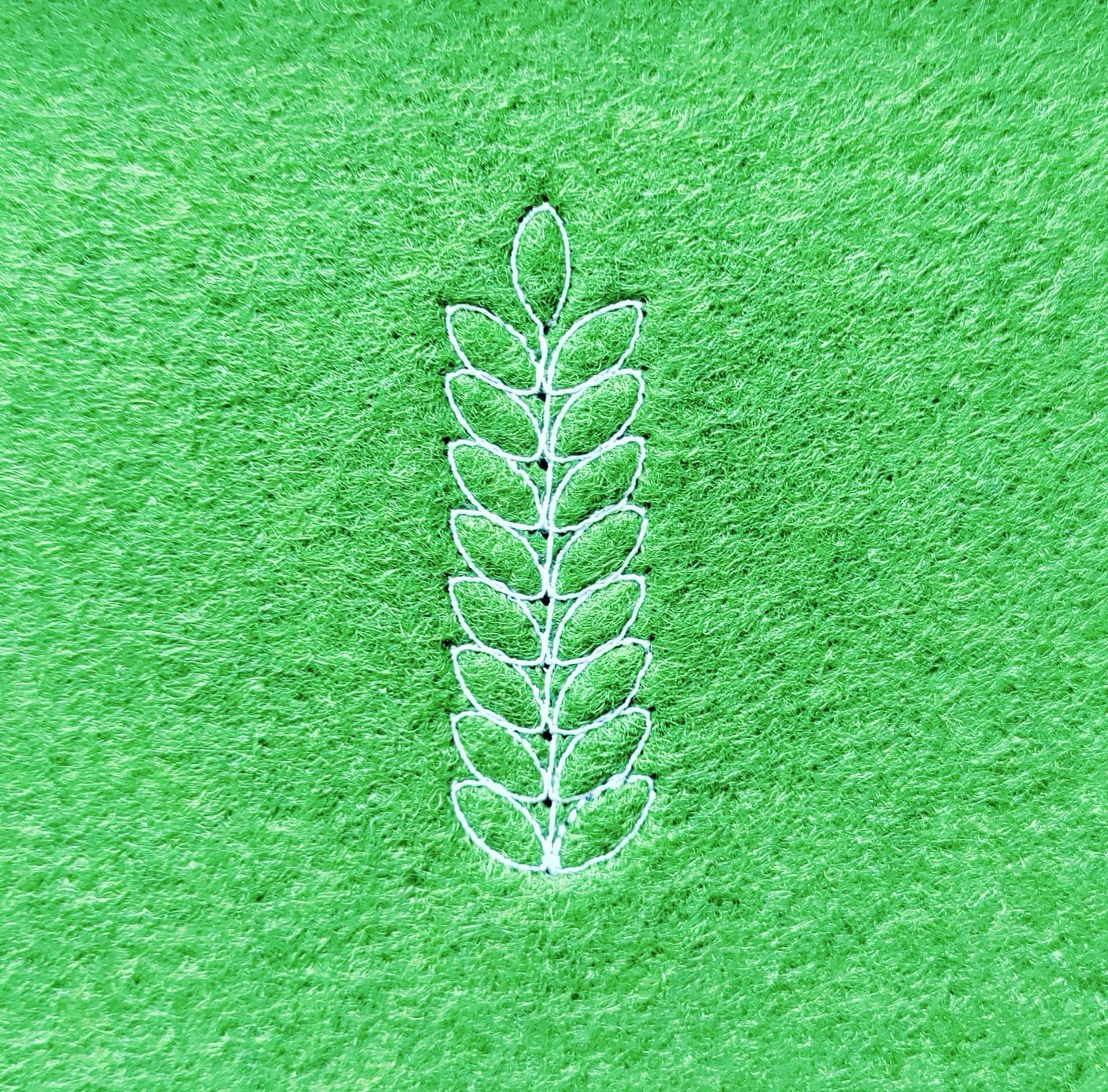 A representation of a stalk of wheat, stitched in white thread on a green felt background.