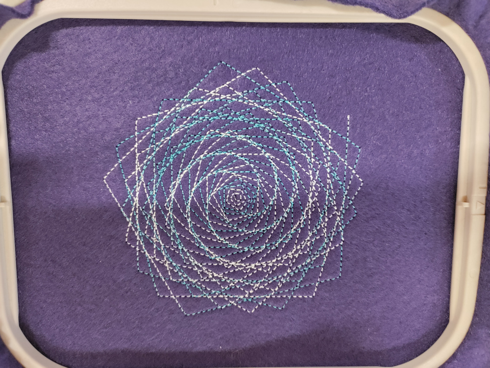 A pattern designed in Turtlestitch and stitched into felt by a digital embroidery machine. It shows a polygons overlapping and getting gradually smaller as they spiral into the centre.