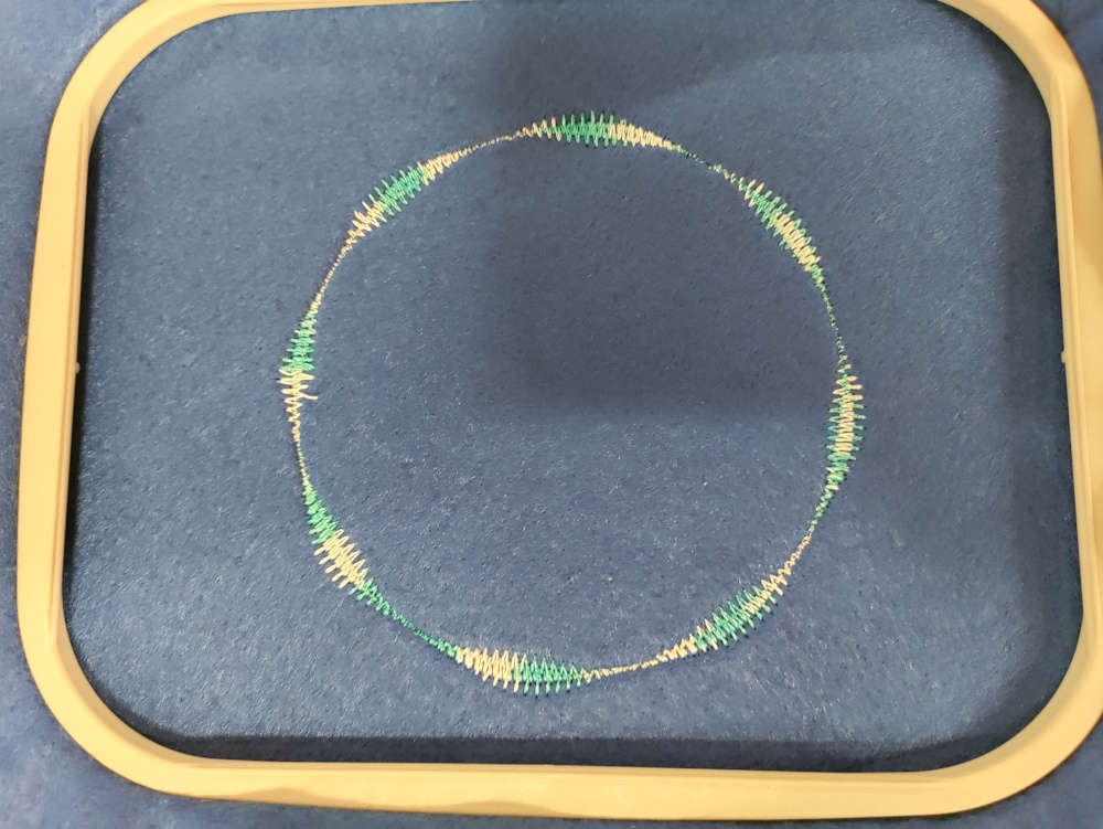 A pattern designed in Turtlestitch and stitched into felt by a digital embroidery machine. It shows a circle with overlapping lines of thread.