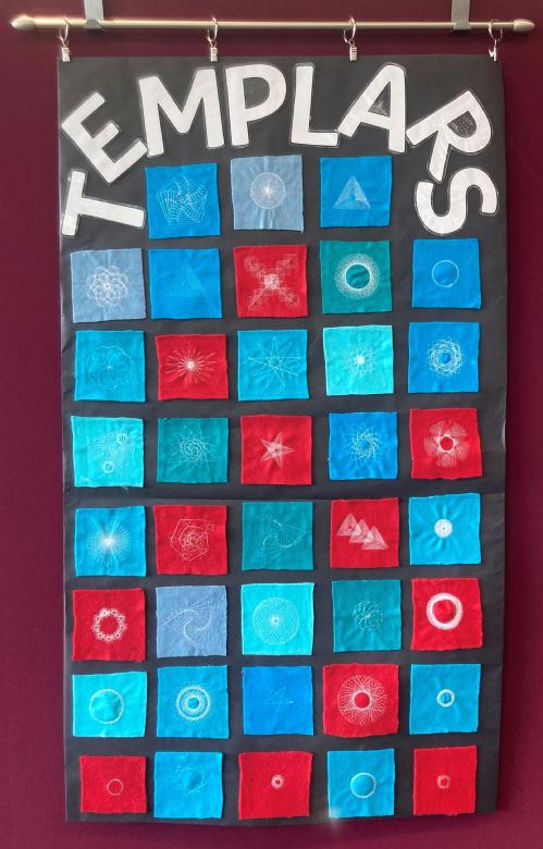 A collage of blue, red and turquoise felt fabric squares mounted on black paper. The squares have white embroidery on them and the school name, Templars, at the top of the collage. The collage hangs from a horizontal pole. 