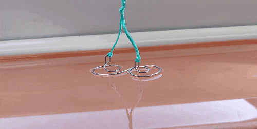 a short clip showing the surface tension formed between a wire and the water surface. When the wire is raised up the water appears to snap and falls back into the bowl below.