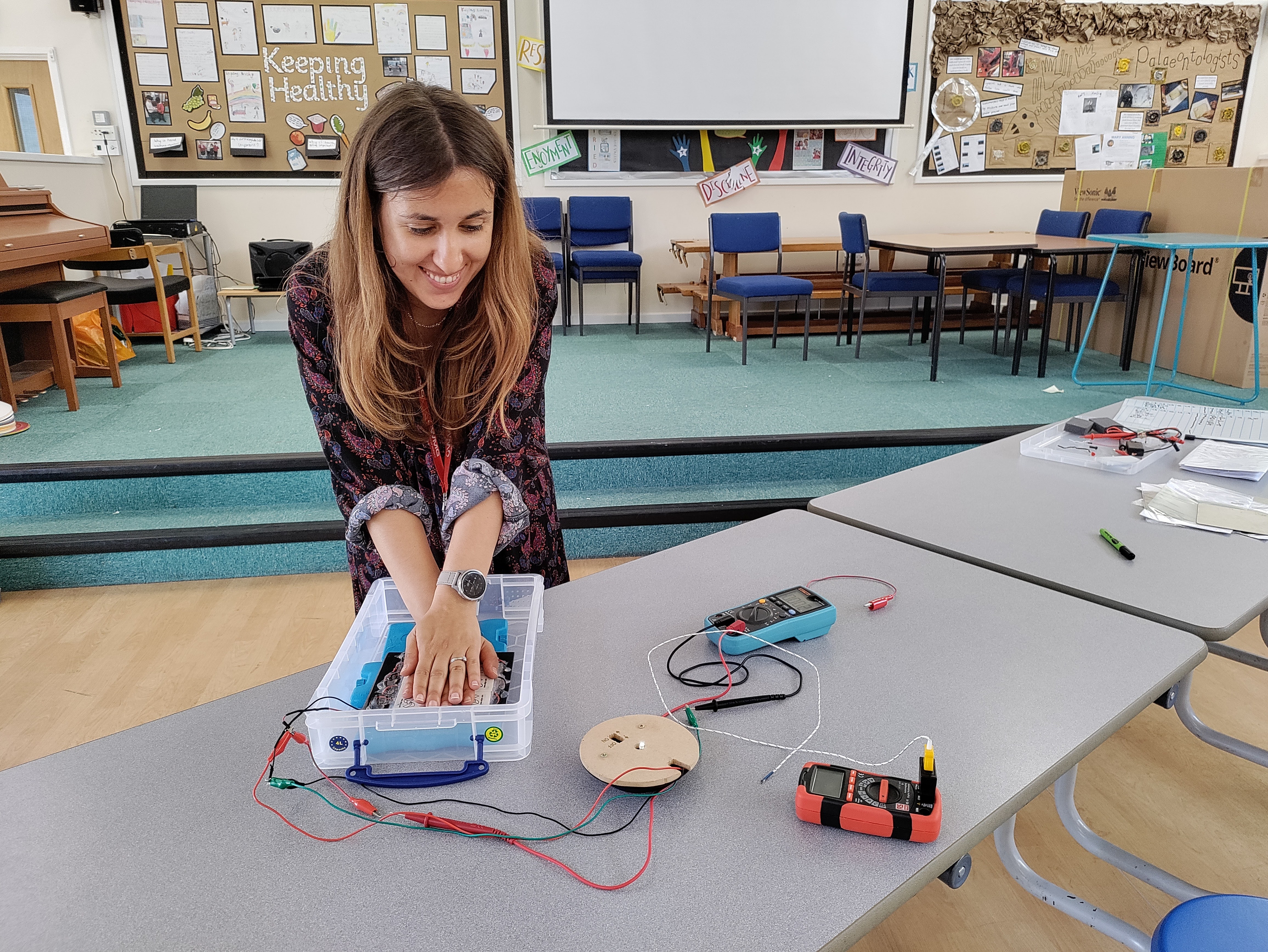 Dr Antonia pressing her hands on an thermoelectric generator which is connected to a light bulb and a voltmeter,