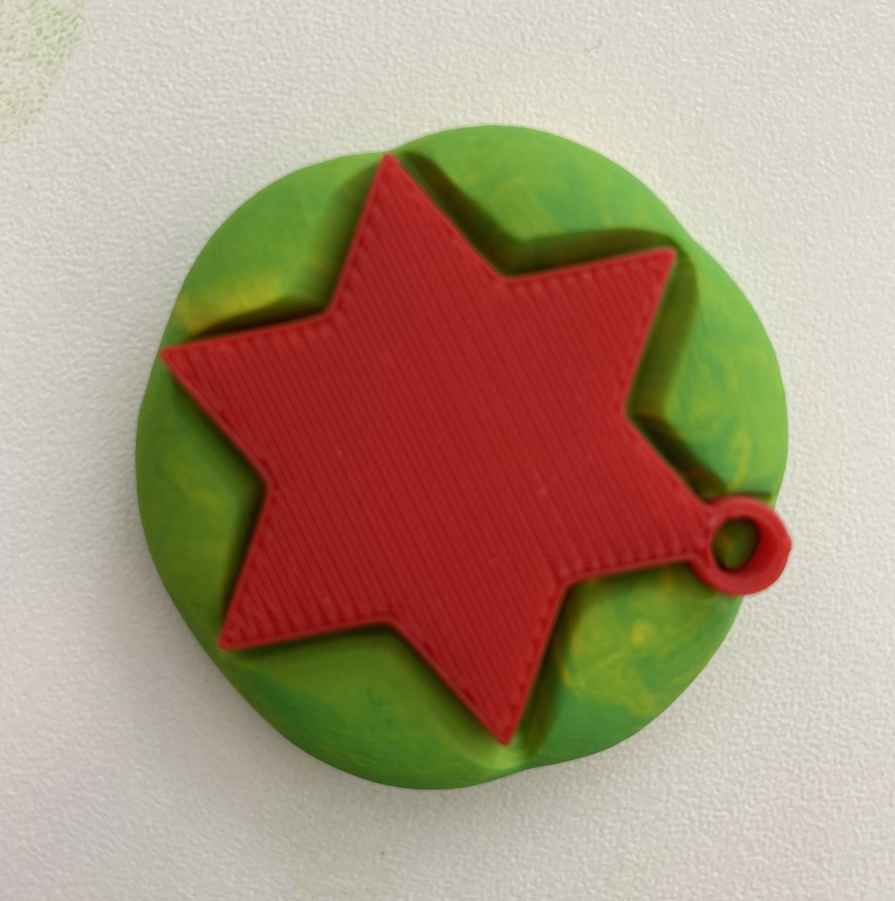 Flat star 3d print pushed into a green ball of playdough 