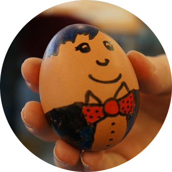 A Hand holding an egg with a face and bowtie drawn on with a marker pen