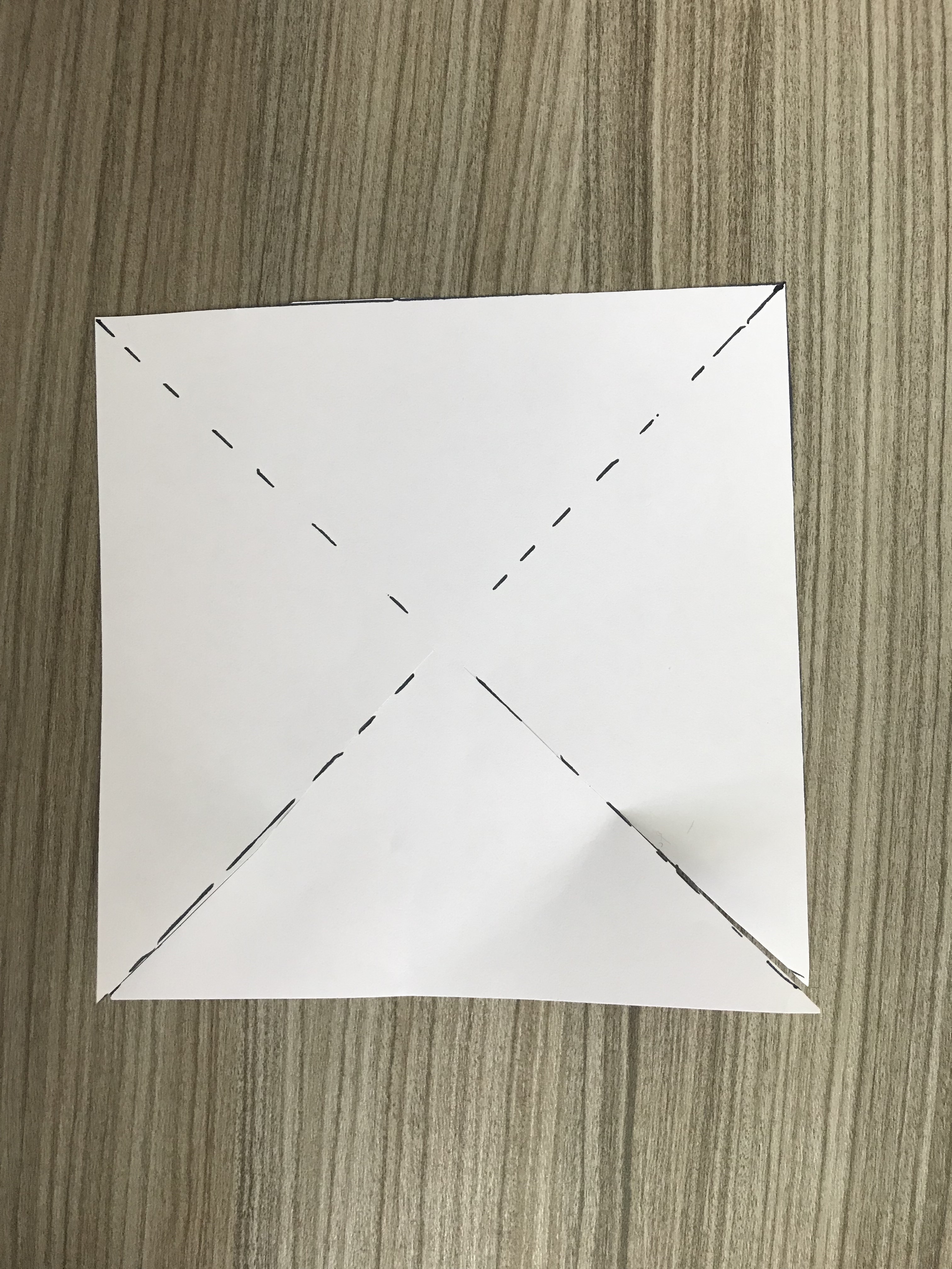 white square piece of paper on a desk with diagonal cuts made through it with a small bit left in the center.