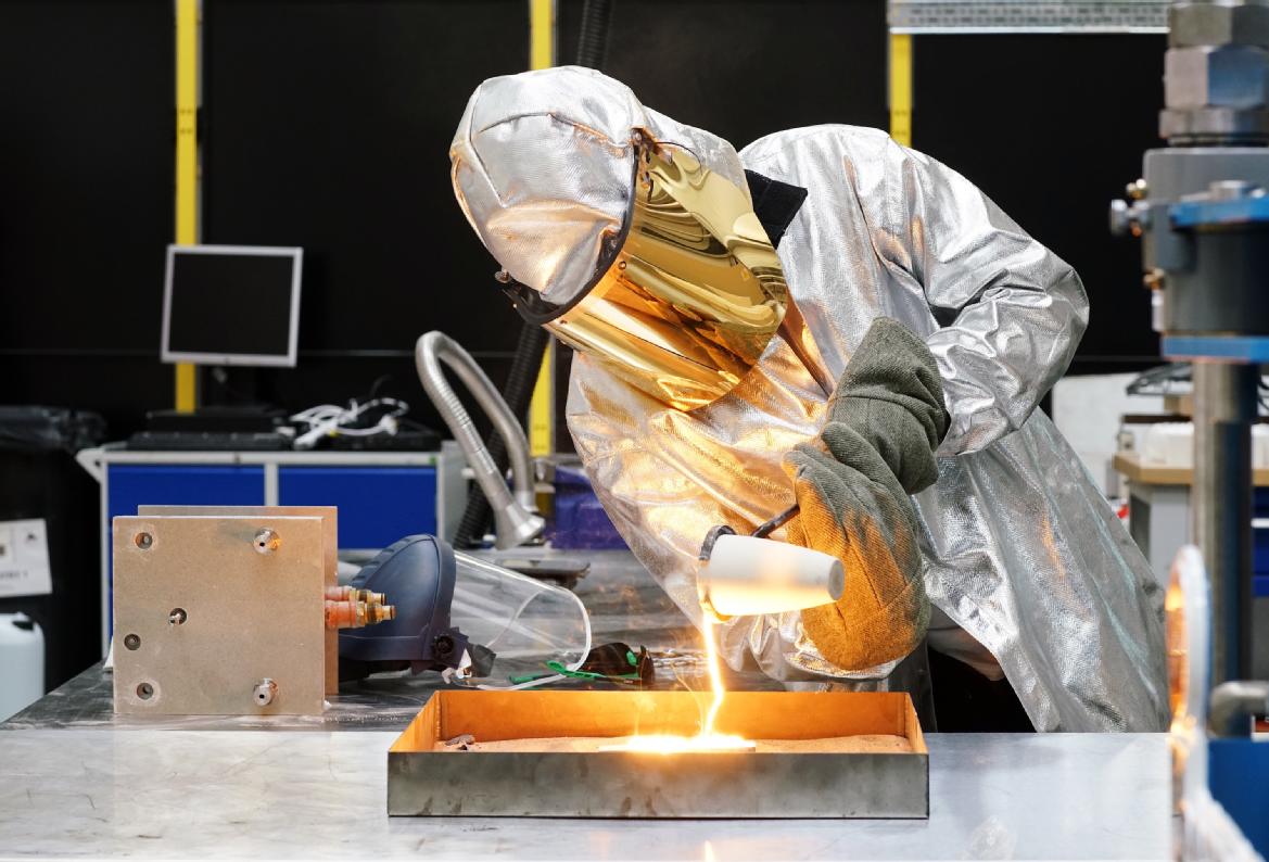 A person in a protective suit pouring molten metal
