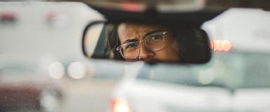 Picture shows driver looking in rear view window to support how road rage really affects driving