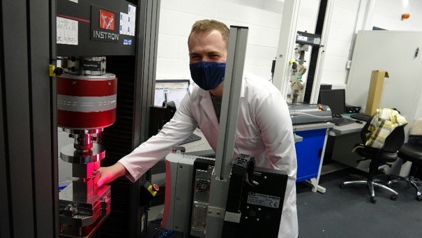 Researcher in white lab coat and face mask operating equipment.