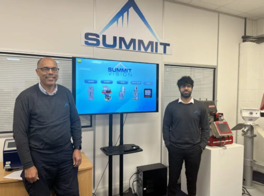 Two employees at Summit smiling by a digital screen.