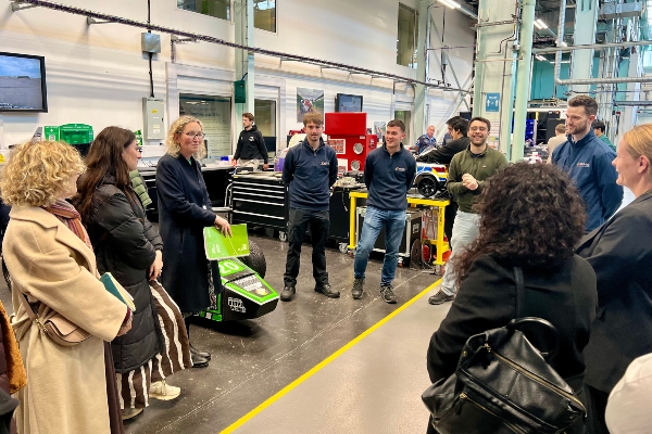 Three technical apprentices present to group of people in an engineering hall. 
