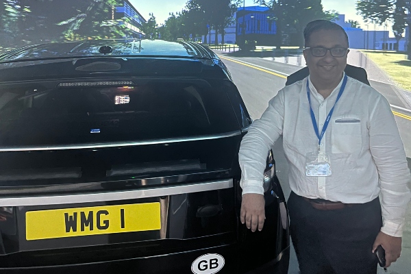 Member of the CII stands smiling inside WMG's driving simulator
