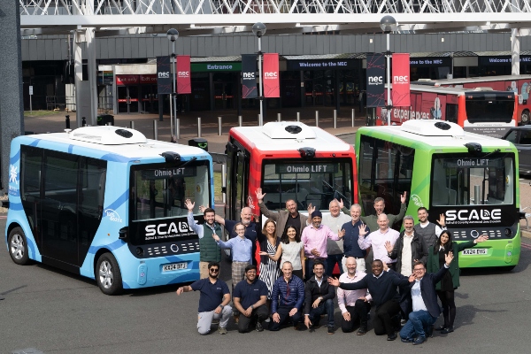 Members of the SCALE project team stand in front of three self-driving shuttle buses.