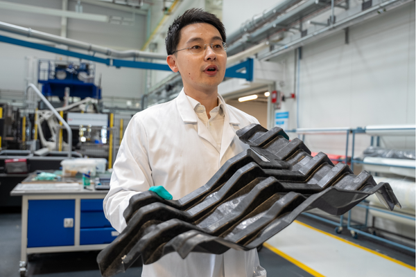 Dr Zhang carries a multi-strand plastic structure inside a laboratory whilst wearing a white lab coat and gloves.